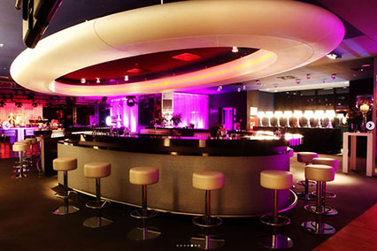 Elegant bar area at the binding.energy event venue with soft pink lighting, white-upholstered seating, and illuminated glassware — creating an inviting atmosphere for cocktails and quiet conversation