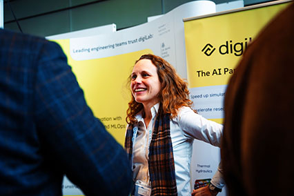 Amanda Niedfeldt, Head of Business Development at digiLab, engages in friendly discussion with interested participants at the binding.energy exhibitor booth, presenting AI-driven solutions for complex engineering challenges in safety-critical sectors