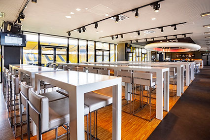 Bright lounge area of the Tivoli stadium in Aachen with white tables and chairs illuminated by daylight through the glass façade — set for the binding.energy conference dinner