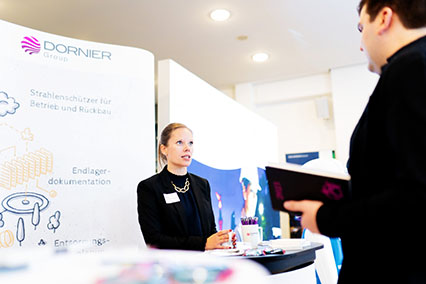 The modern white booth of Dornier Hinneburg at the binding.energy exhibition, with a stand representative in professional exchange with a participant in the brightly lit, architecturally refined exhibition hall
