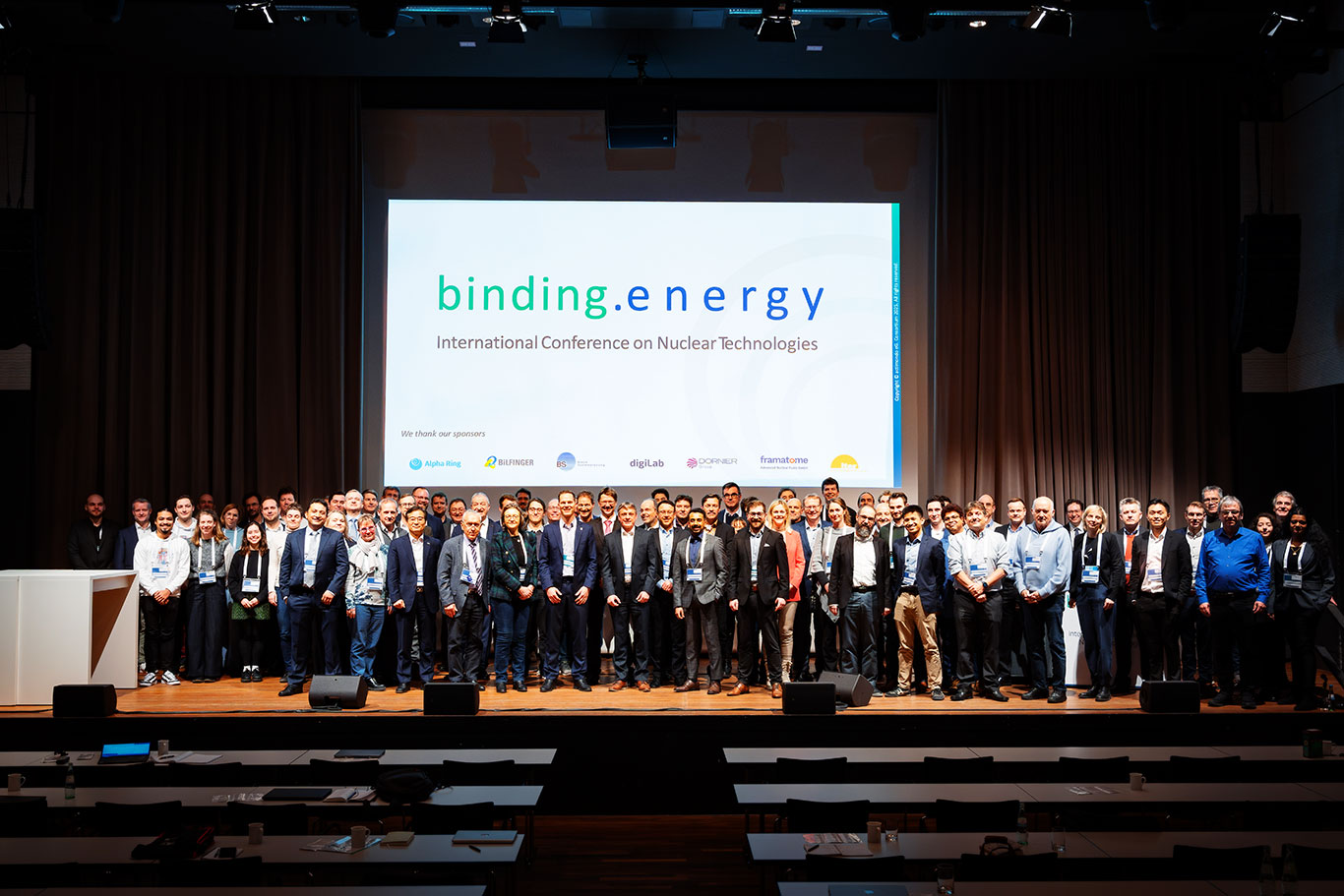 Over 100 participants of the binding.energy International Conference on Nuclear Technologies pose on the main stage, symbolizing collaboration across nuclear fission and fusion sectors