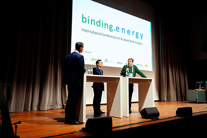 Dr. Alain Bécoulet (ITER Organization) and Dr. Yeong-Kook Oh (Korea Institute of Fusion Energy) in expert panel discussion on fusion technology at binding.energy International Conference, with moderator and conference banner on main stage