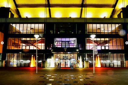 Impressive night view of the Tivoli Aachen entrance with illuminated glass facade and glowing yellow roof — a signature location for the binding.energy evening program