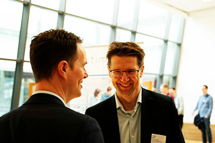 Torsten Pfalz, Segment Manager for Nuclear Safety and Radiation Protection at TÜV Rheinland, smiles in conversation with a colleague in the bright conference lobby at binding.energy
